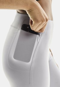 Hoge taille witte leggings gemaakt van rekbaar materiaal, met een zijzak voor een smartphone en een minimalistisch ontwerp met een gladde textuur.