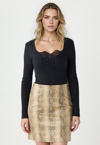 Czarna bluzka z długim rękawem z koronkowymi detalami przy dekolcie, zestawiona z dopasowaną, błyszczącą spódnicą w złoto-brązowy wzór w węża.