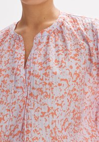 Blusa viola chiaro con un motivo arancione astratto, presenta un collo a V e dettagli arricciati. Tessuto strutturato con una vestibilità morbida.