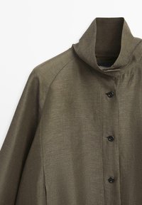 Hnědý kabát s texturou, stojacím límcem a třemi předními knoflíky, zobrazený na bílém pozadí s viditelnými švy na rameni a rukávu.