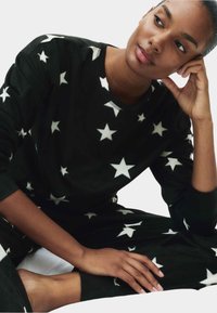 Zwarte fleecie loungewear set met witte sterpatronen. Het bovenstuk heeft een ronde hals en lange mouwen, terwijl de broek elastische boorden heeft.