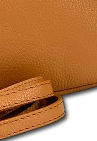 Dichte close-up van een tan leren handtas, met een gestructureerd oppervlak, gerolde handvatten en zichtbare stiksels langs de randen.