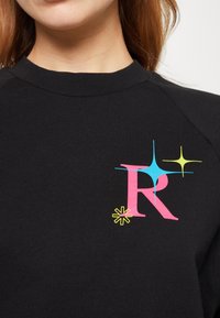 Felpa nera con collo rotondo, caratterizzata da un design grafico colorato. Il design include una "R" rosa e forme di stelle luminose in blu e giallo.