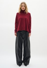 Pull à col roulé rouge à coupe décontractée avec des poignets côtelés, associé à un pantalon large en cuir noir avec une texture lisse et des coutures.