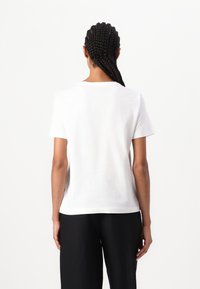 Witte katoenen t-shirt met een ronde hals en korte mouwen, met een rechte snit en minimale naden, gedragen met zwarte broek.