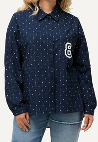 Navy blue button-up shirt with white polka dots and vertical lines, featuring a pocket with an embroidered number "8." Long sleeves with button cuffs.