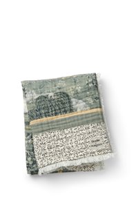 Mønstret tæppe med bløde grønne og hvide nuancer, botaniske designs, frynsekant og et mærke med teksten "Elodie x Morris & Co."