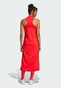 Red, sleeveless dress with a fitted bodice and long skirt, featuring side black stripes. Paired with red socks and white athletic shoes.