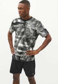 Svart och vit mönstrad kortärmad skjorta med rund halsringning, tillsammans med svarta shorts. Tyget visar ett texturerat, abstrakt mönster.