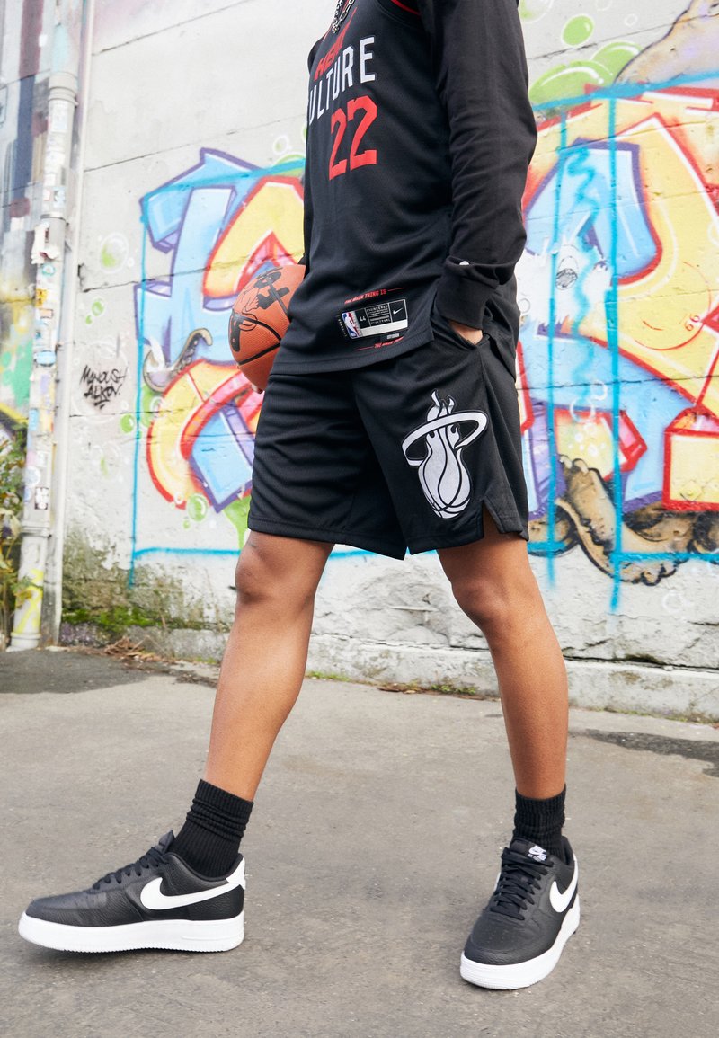 Fekete kosárlabda mez piros részletekkel és 22-es számmal, fekete rövidnadrággal, amelyen a Miami Heat logója látható, és fekete Nike tornacipővel.
