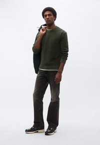 Zelen pulover z rebrasto strukturo, sive kavbojke, nosi temno zeleni suknjič. Obutev je v mornarsko modri, rumeni in krem barvi ter ima robustno zasnovo.