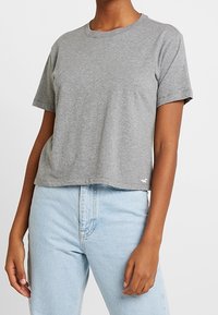 Grå t-shirt med kort ärm i mjuk bomull, med rundad halsringning och avslappnad passform. Litet vitt logotypdetalj vid fållen.