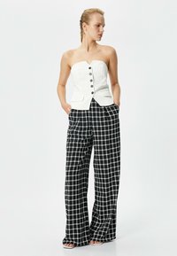 Top blanc sans bretelles avec un corsage ajusté et des boutons noirs, associé à un pantalon à pattes d'éléphant noir et blanc à carreaux. Texture lisse et coupe ajustée.