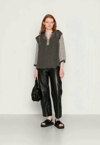 Blusa preta e branca com padrão, com mangas rufadas, combinada com calças de couro pretas, sandálias pretas e uma mala texturizada preta.