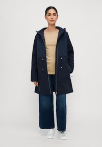 Marineblauwe gewatteerde parka met capuchon, met een ruitpatroon op de schouders, contrasterende blauwe panels, ritsluiting en twee voorzakken.