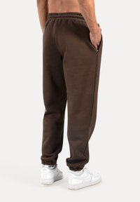 Braune Sweatpants mit elastischem Bund und Bündchen, ausgestattet mit Seitentaschen. Getragen mit weißen Sneakern. Glatte Textur, lässiges Design.