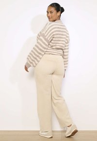Bež ribane kordurojske hlače visoke pasu, v kombinaciji s svetlobno črtasto pleteno jopico v mehkobnih bež in kremnih tonih.
