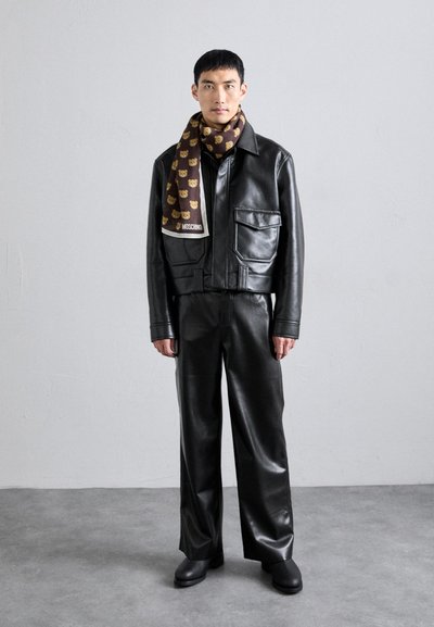 Jachetă din piele neagră cu un design scurt, buzunare mari și pantaloni asortați. O eșarfă maro cu modele de urși este purtată în jurul gâtului.
