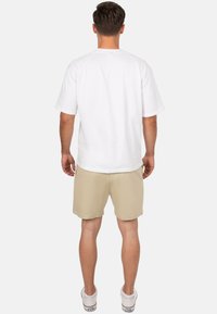 T-shirt bianco a maniche corte abbinato a pantaloni corti color khaki. La t-shirt ha una vestibilità morbida e i pantaloni sono di lunghezza al ginocchio con una texture liscia.