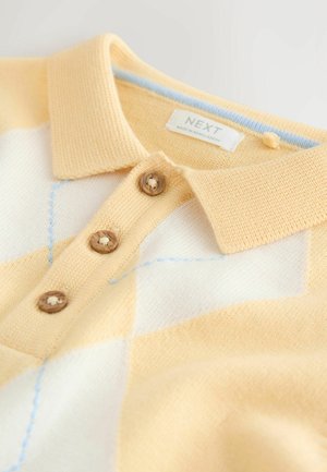 Gul og hvidstrikket polo med tre træknapper, en foldet krave og lyseblå stingdetaljer. Mærket viser "NEXT."