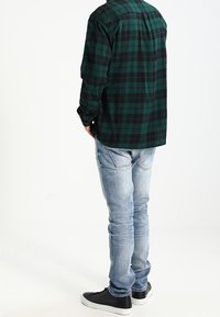 Zeleno-černé kostkované košile, zapnutá, s uvolněným střihem, spárovaná s světle modrými džíny a černými teniskami, pohled zezadu.