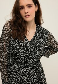 Vestido negro con mangas globo transparentes, que presenta un patrón repetido de manchas de leopardo gris y calaveras, con una cintura ajustada.
