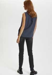 Bezramenný námořnický top vyrobený z lehké tkaniny, spárovaný s úzkými černými džíny a robustními černými botami. Jednoduchý design s jemným detailem na zadní straně.