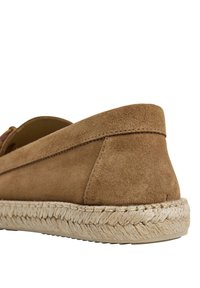 Escarpin en suède de couleur beige avec un talon plat. Présente des détails en corde de jute le long de la semelle et un design simple avec des accents minimalistes.