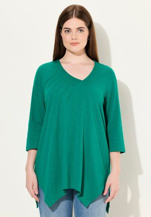 Top verde, leggero, con maniche a tre quarti e scollo a V; presenta pieghe decorative sulla parte anteriore e un orlo asimmetrico leggermente curvo.