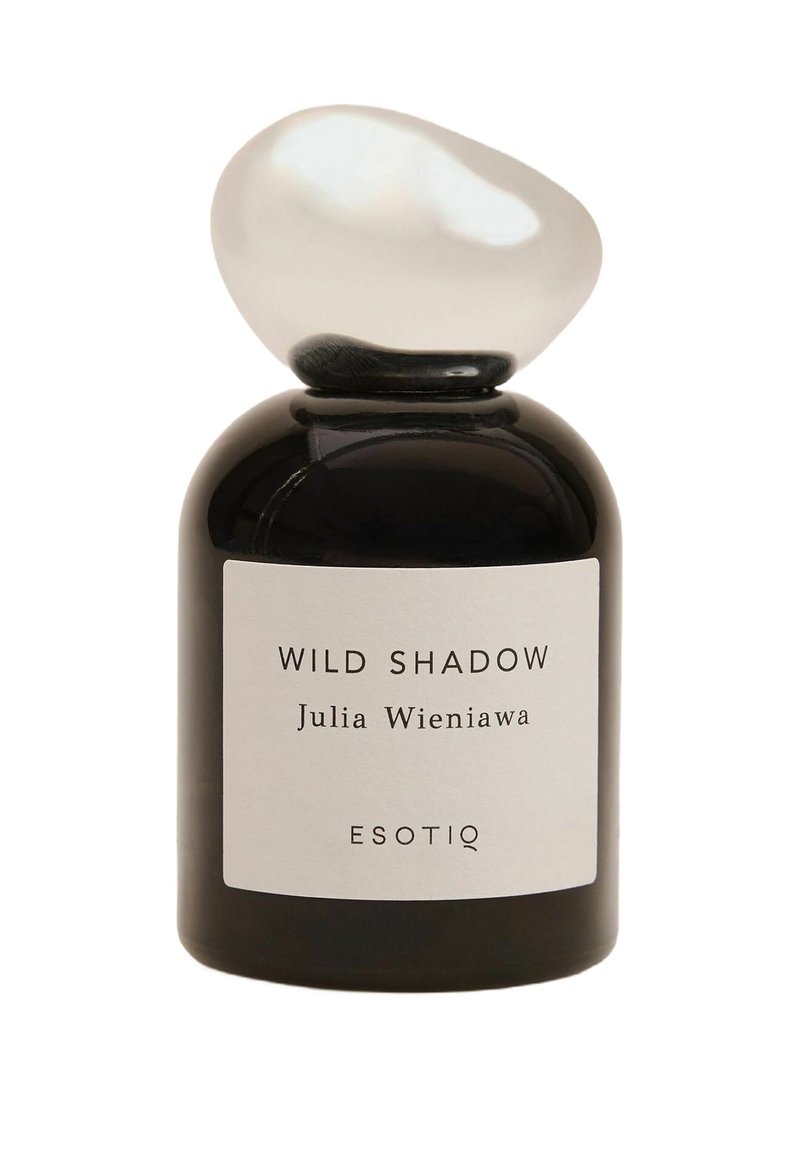 Czarny szklany flakon perfum o zaokrąglonym kształcie, z gładką, owalną białą nakrętką. Etykieta z napisem "WILD SHADOW" oraz "ESOTIQ".