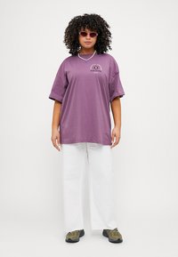 Purple oversized t-shirt with short sleeves and a graphic print on the chest, paired with white wide-leg trousers and green sneakers.