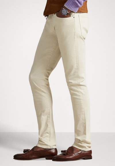 Bež hlače uskog kroja od pamuka, s pet džepova i detaljima sa bočnih šavova, uparene s smeđim kožnim mokasinama.