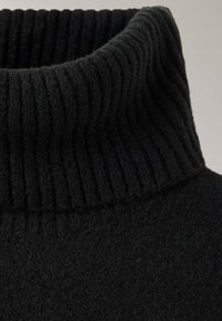 Col de pull à col roulé en tricot côtelé noir avec un tissu doux et texturé en gros plan.