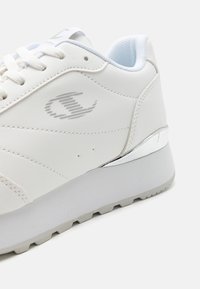 Witte sneaker van glad leer met een textuurpatroon en zilveren accenten op de hiel. Voorzien van witte veters en een gevoerde binnenkant.