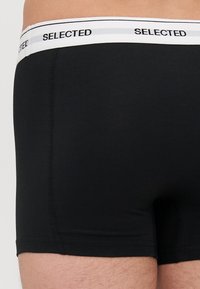 Black underwear in a fitted design, featuring a white waistband with "SELECTED" text. Soft texture with seamless edges. Suitable for everyday wear.