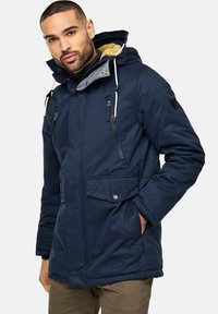 Marineblå parka-jakke med hætte, lynlåslommer og fleece-foring. Har snoretræk og struktureret stof til isolering.
