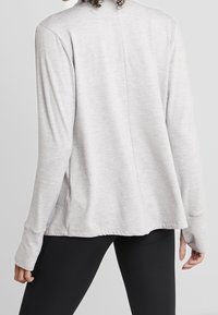 Maglia a maniche lunghe grigia chiara con vestibilità rilassata, texture morbida, orlo arrotondato e spacchi laterali; presenta dettagli di cucitura lungo la parte posteriore.