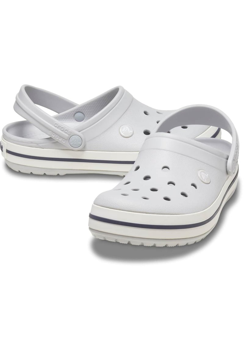 Zuecos ligeros blancos con punta cerrada, agujeros de ventilación y una correa trasera. Con una suela bicolor que presenta una franja de acento oscuro.