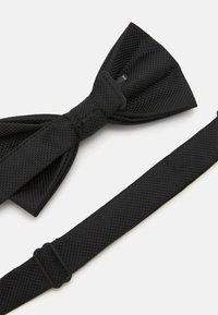 Nœud papillon noir en tissu texturé avec un motif tissé. Comprend une sangle réglable avec une boucle en plastique. Design compact et symétrique.