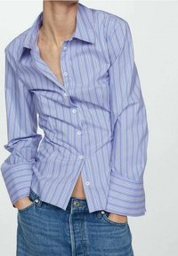 Chemise boutonnée bleu clair avec des rayures blanches verticales. Présente un col classique, des manches longues et une coupe légèrement décontractée.