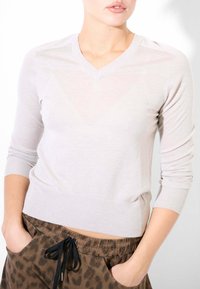 Maglione grigio chiaro con scollatura a V, maniche lunghe aderenti e polsini a costine. Indossato sopra pantaloni a stampa leopardata marroni.