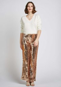 Pull en tricot blanc à col en V associé à un pantalon large en sequins rose doré, présentant une surface brillante et texturée, et des sandales neutres.