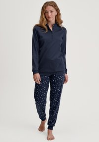 Marineblauwe lange mouwen top met knoopsluiting en marineblauwe pyjamabroek met een maan- en sterrenpatroon, gemaakt van zachte stof met manchetten.