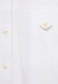 Primo piano di un tessuto di camicia bianca, con una tasca a pattina bottone a destra e tre bottoni visibili su una patta a sinistra.