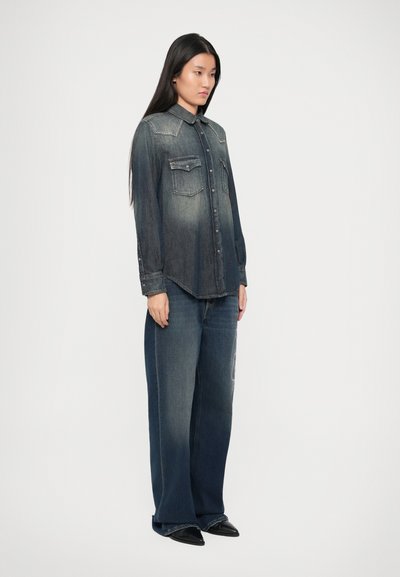 Denim shirt met een kraag, vervagend van donkerblauw naar lichtblauw, met twee borstzakken en studaccenten. Gepaard met een wijde dark jeans.