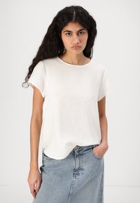 Top bianco a maniche corte con scollatura rotonda e orlo leggermente curvato, realizzato in un tessuto leggero e testurizzato. Indossato con una gonna di jeans.