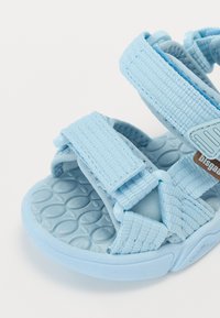 Blaue Stoffsandalen mit verstellbaren Riemen, einer strukturierten Gummisohle mit ovalem Muster und einem Markenakzent.
