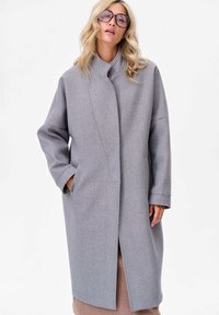 Manteau en laine gris avec un col montant, des manches longues, des poches latérales et une silhouette droite. Présente une texture subtile et un design minimaliste.