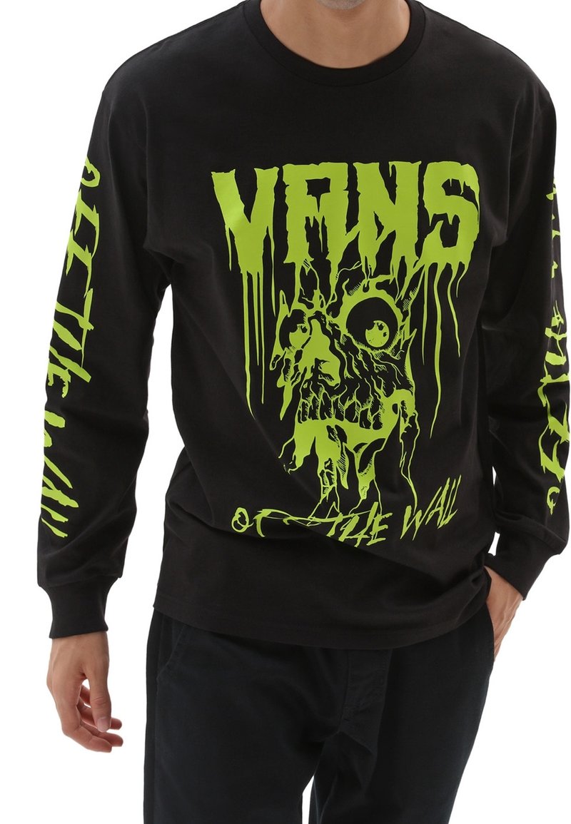 Personne portant un t-shirt noir à manches longues avec un texte vert vif dégoulinant "MRKS" et un graphique de crâne à l'avant, ainsi qu'un texte assorti sur les deux manches.