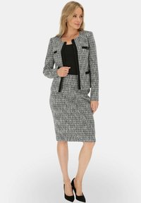 Szary garnitur z tweedu, składający się z dopasowanej marynarki z czarnymi akcentami oraz ołówkowej spódnicy sięgającej do kolan, zestawiony z czarnymi szpilkami.
